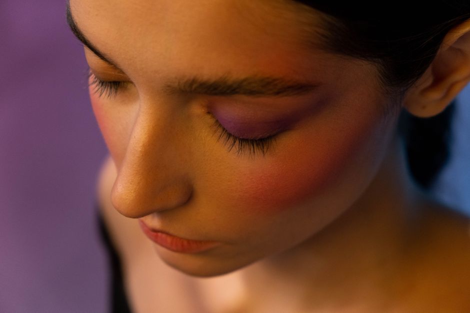 Artistic close-up portrait showcasing bold makeup blending blush and purple eyeshadow.