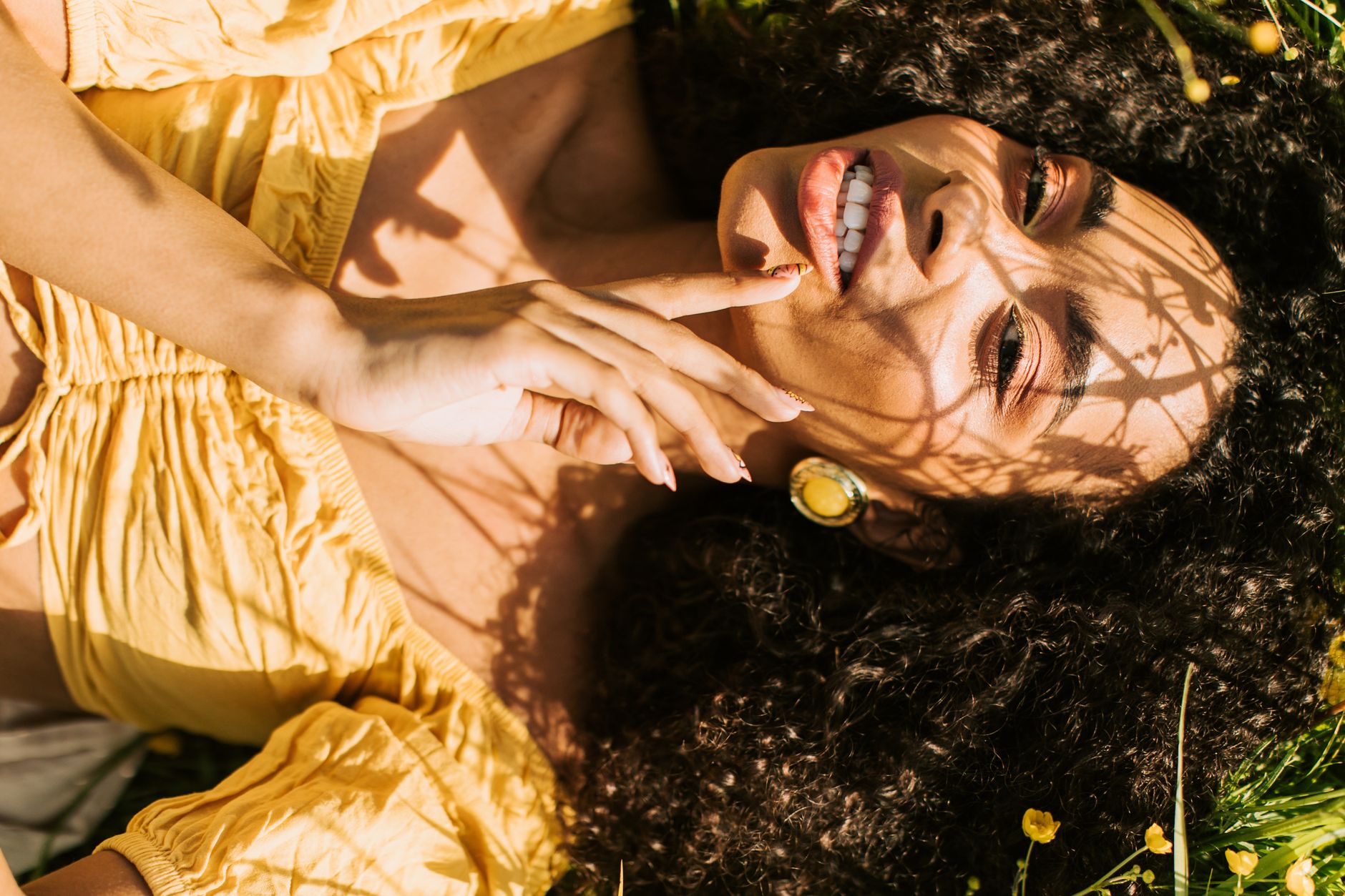 Beautiful woman with curly hair lying on grass in sunlight, creating playful shadow patterns on her face.
