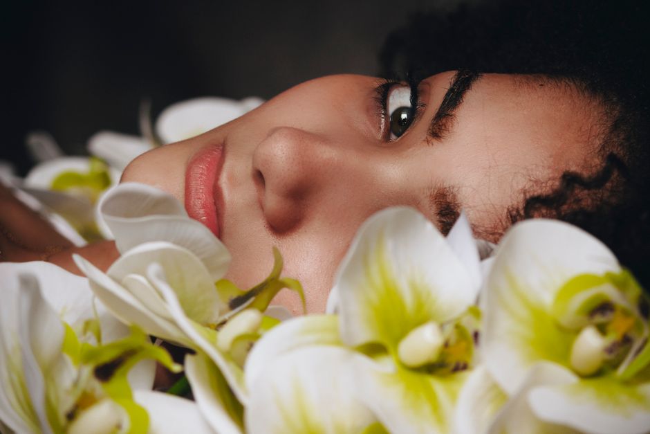 A serene portrait of a woman surrounded by white and green orchids in close-up.