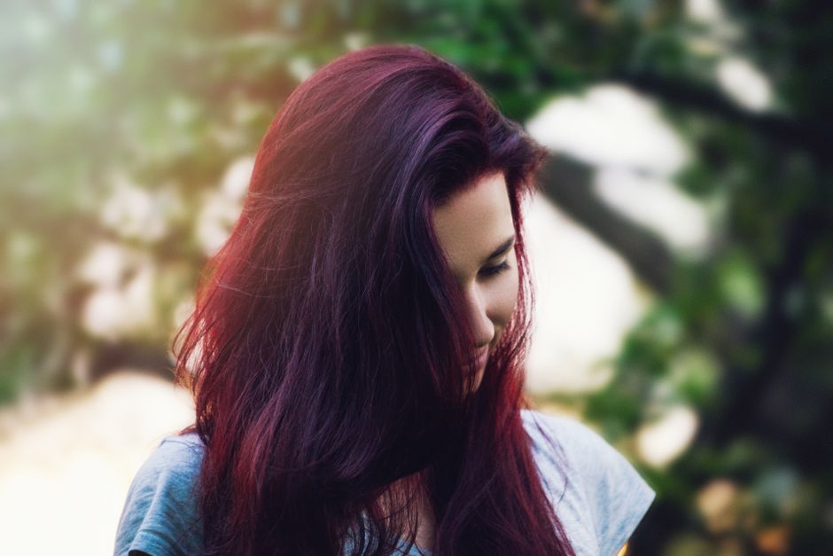 A thoughtful portrait of a young woman with vibrant red hair outdoors.