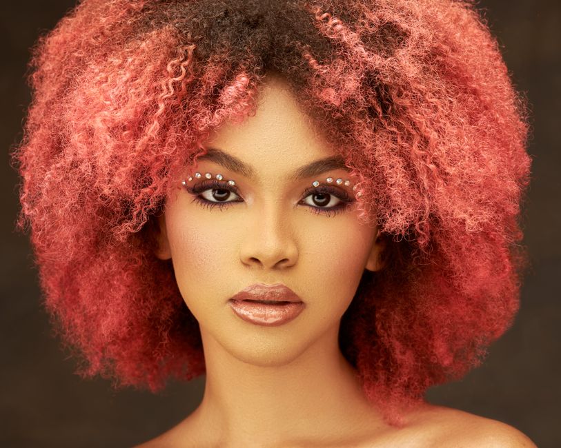 Captivating portrait of a woman with pink curly hair and artistic makeup.