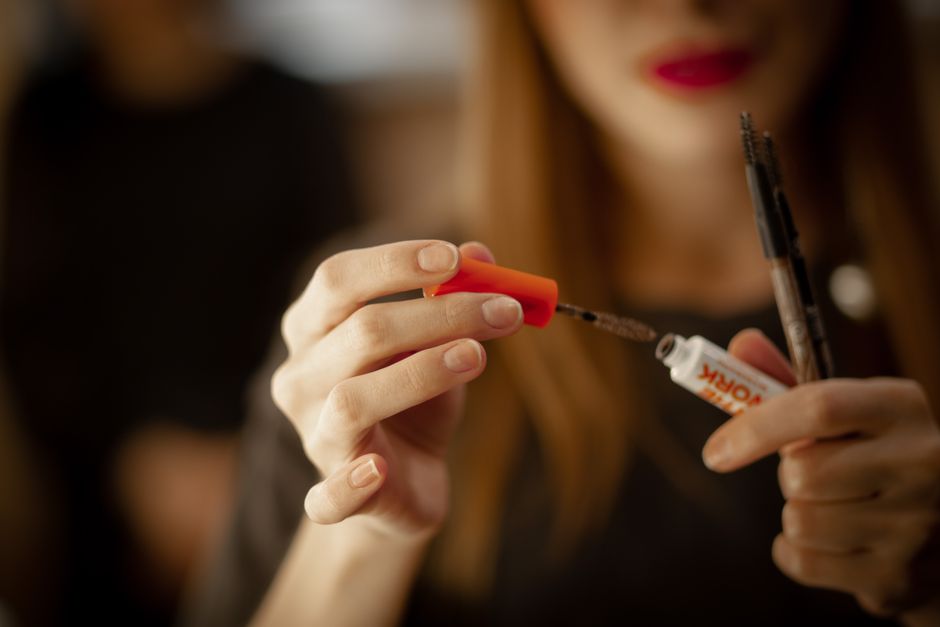 A woman focuses on applying mascara using a brush, emphasizing eye makeup detail.