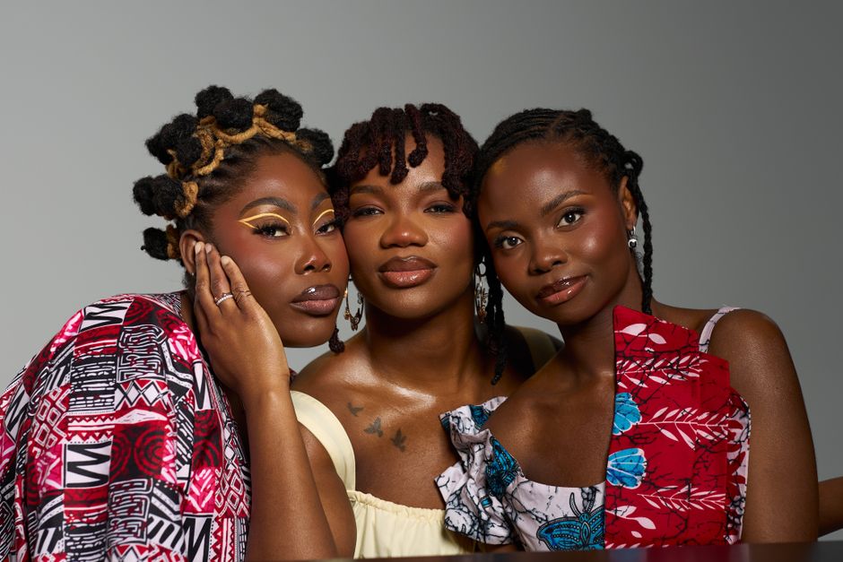 Vibrant portrait of three fashionable women showcasing natural hairstyles and elegant fashion in a studio setting.
