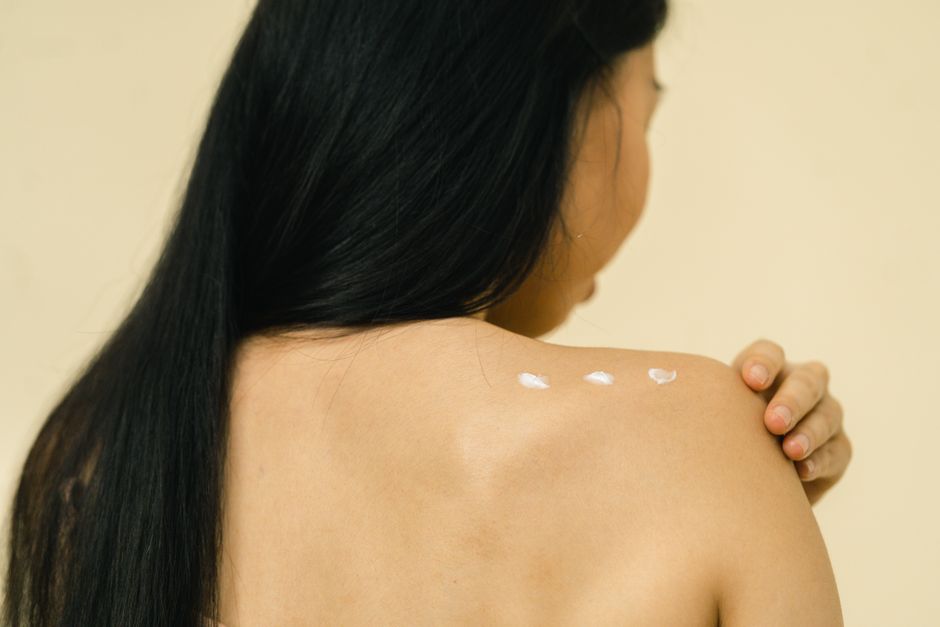 Close-up of a woman applying skincare cream on her shoulder in a studio setting.
