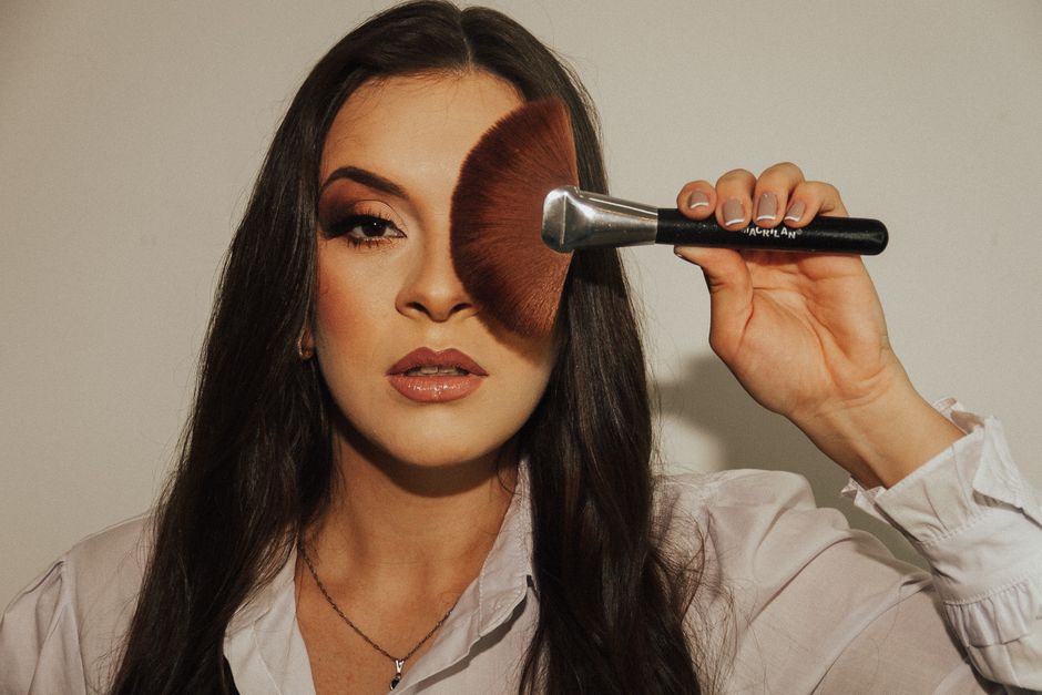 Close-up portrait of a woman holding a makeup brush over her eye, showcasing makeup and beauty concepts.
