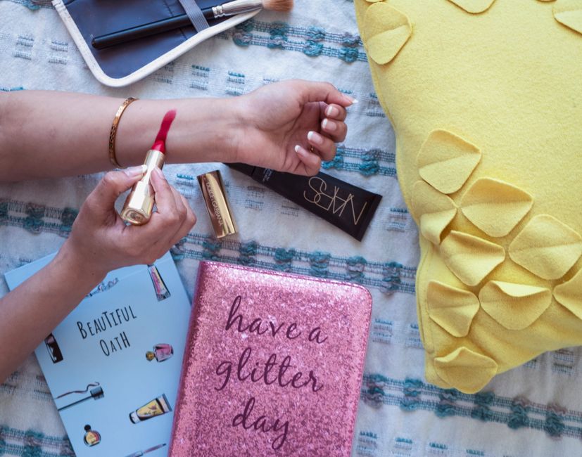 A stylish flat lay of makeup, book, and fashion accessories displaying vibrant colors.