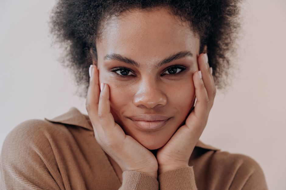 Close-up portrait of a smiling woman with natural afro hair and a soft expression.