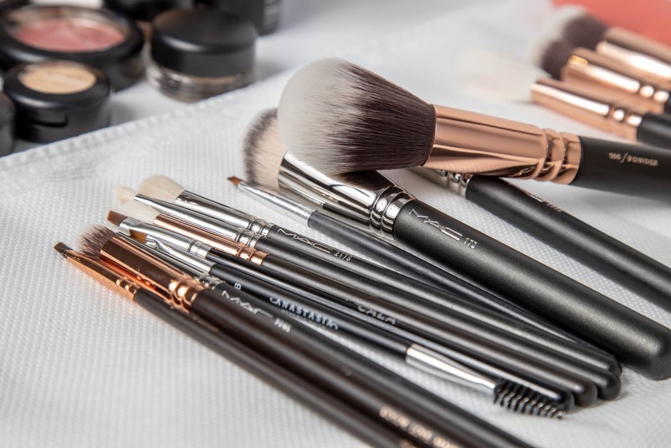 Close-up of assorted makeup brushes on a white cloth with cosmetic products.