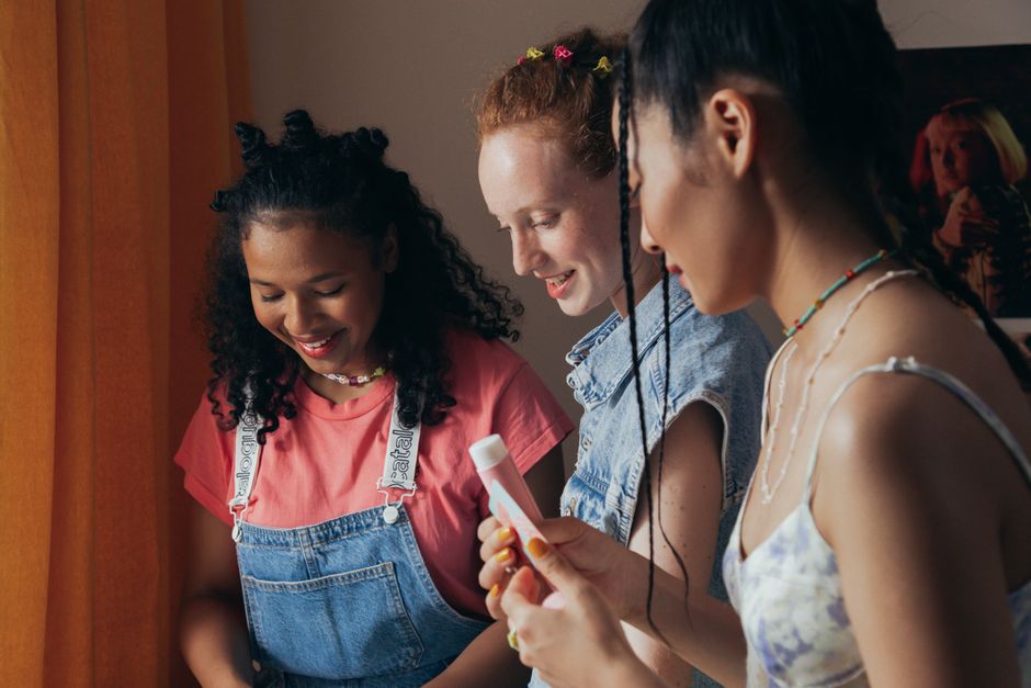 Three diverse women smiling and enjoying a skincare session indoors.