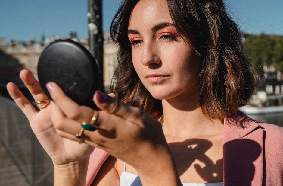 A woman in a pink blazer applying makeup outdoors with confidence and style.