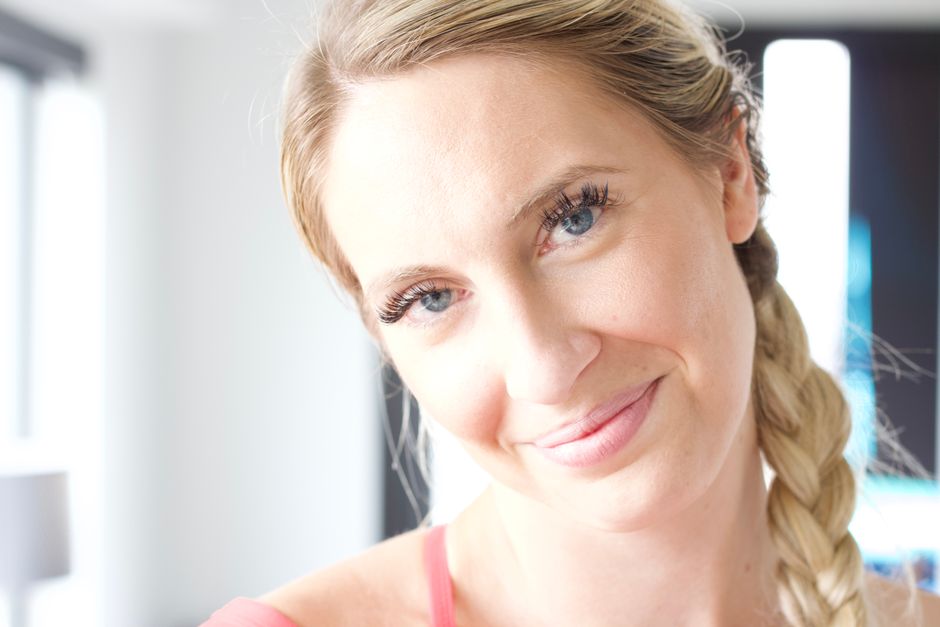 Close-up portrait of a smiling woman with braided hair in a brightly lit indoor setting.