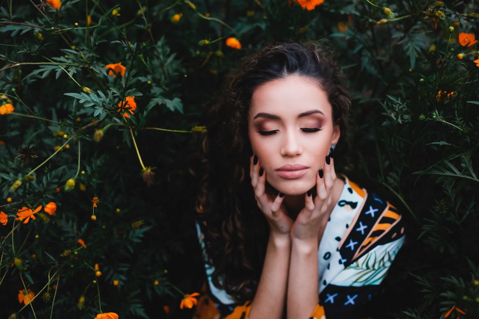 A woman with closed eyes amidst vibrant orange flowers, exuding calmness.