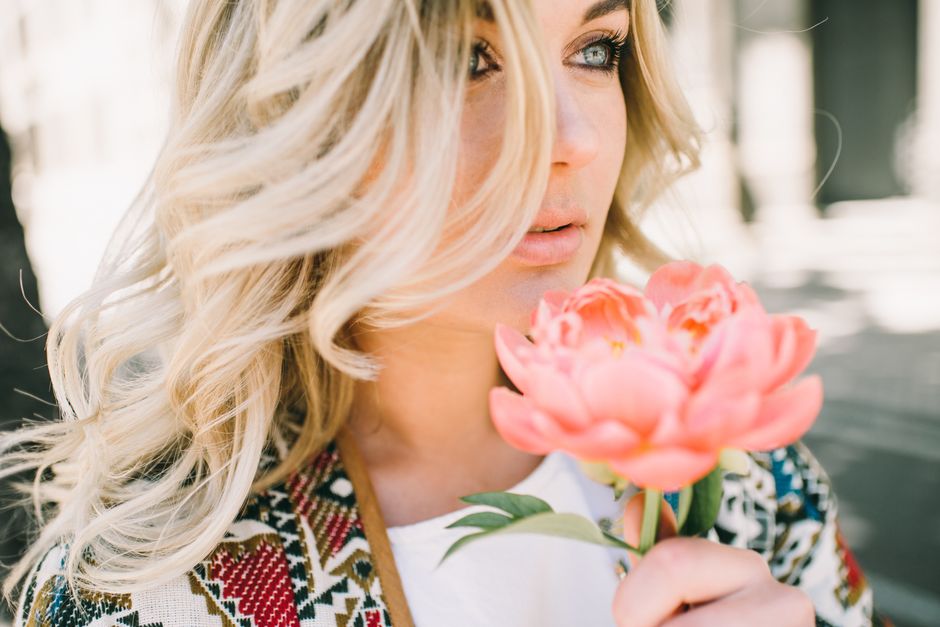 Close-up of a blonde woman holding a pink flower, showcasing beauty and nature.