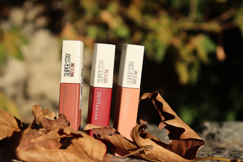 Three Maybelline Super Stay Matte Ink lipsticks among fall leaves, highlighting beauty essentials.
