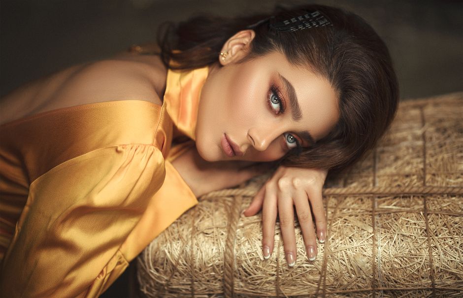 Portrait of a woman in elegant golden silk attire, lying gracefully on textured surface.