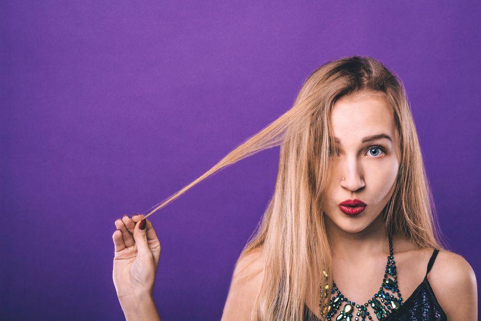 Flirty female with pouting red lips touching hair looking at camera with surprised glance against violet background
