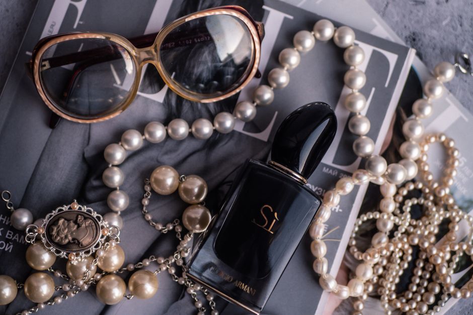 Chic arrangement of pearls, perfume, and sunglasses on a magazine.