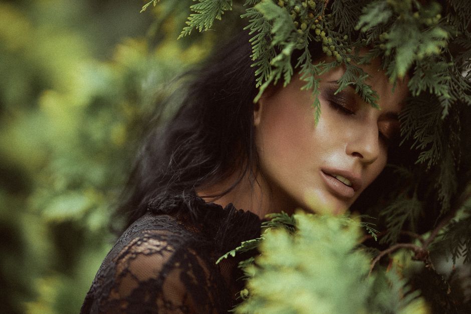 A serene close-up of a woman with eyes closed, enveloped by lush green leaves.