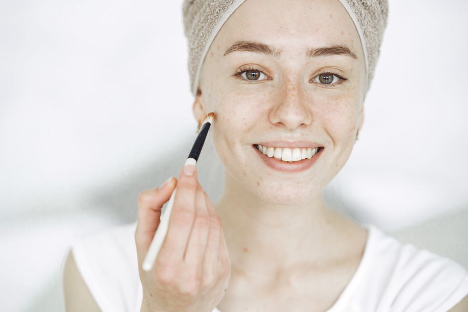 Close-up of a smiling woman applying makeup with a brush, enhancing natural beauty.