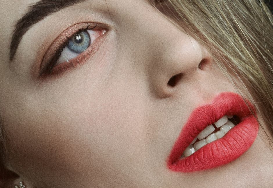 Intimate close-up shot showcasing vibrant red lipstick against fair skin with piercing blue eyes.